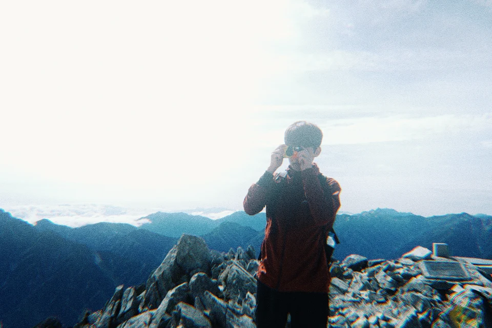 山頂でカメラを構える人と青い山並み